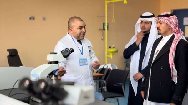 عضو هيئة تدريس من قسم علم الأمراض يشرح استخدام المجهر لطلاب المدارس الزائرين