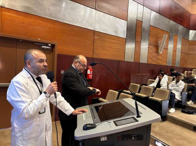 متحدث يخاطب طلابًا بالمعاطف البيضاء في القاعة